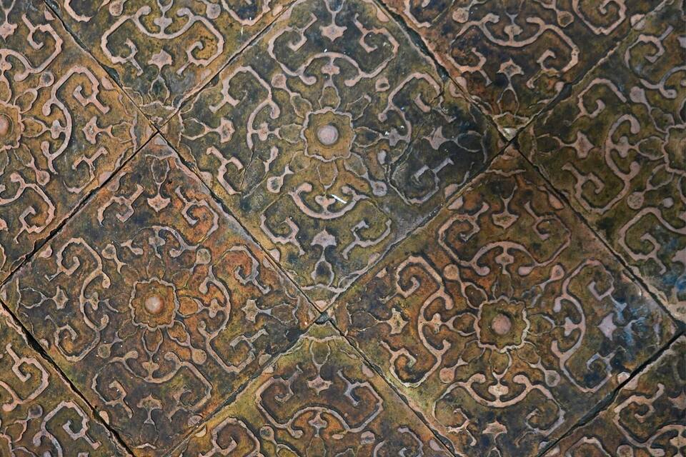 Un disseny de rajola detallat i ornamentat, amb motius intricats i un aspecte desgastat.