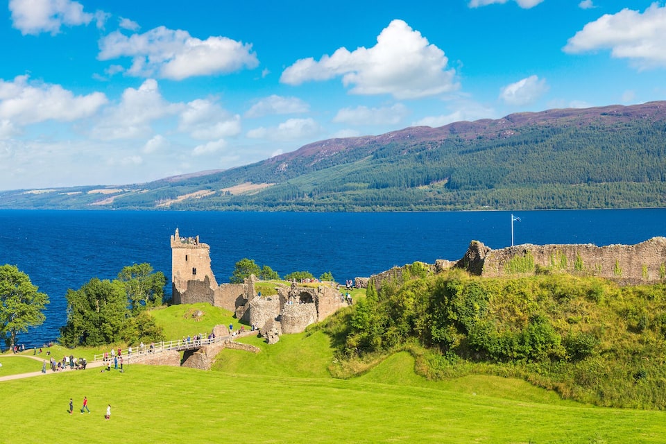 A historic castle on a grassy hill overlooking a large body of water.