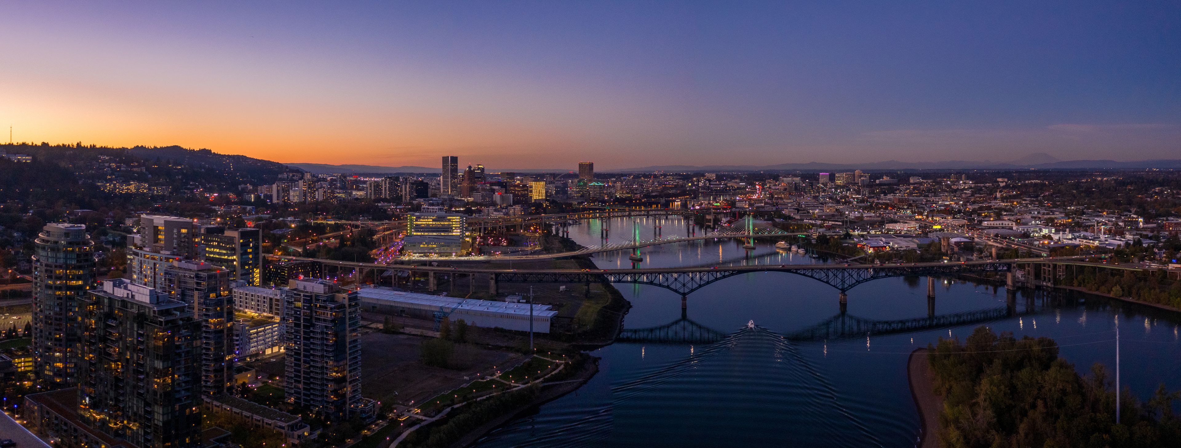Une vue d’une ville au crépuscule, avec une rivière, des ponts et des bâtiments illuminés.