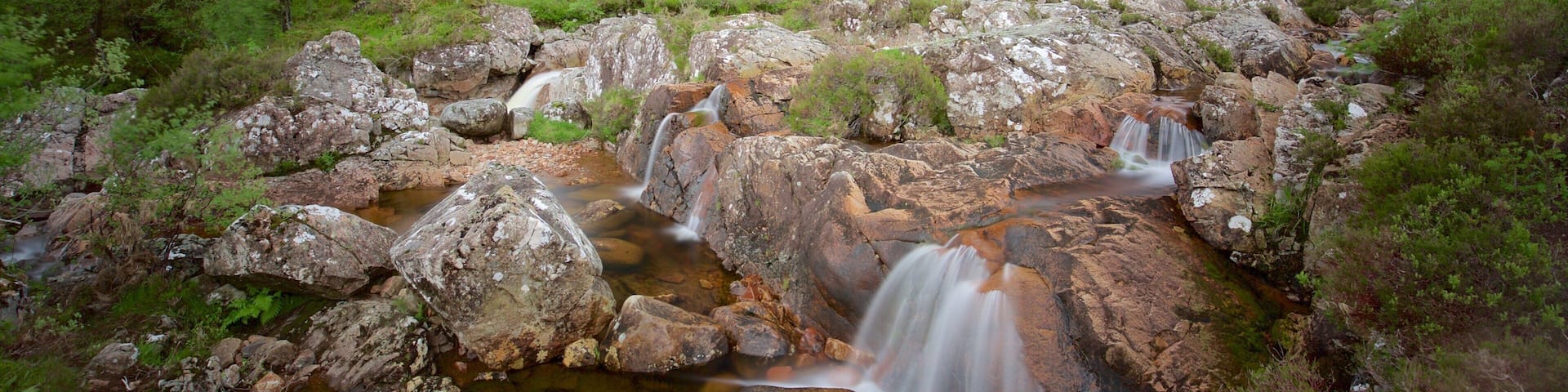 A waterfall cascading over rocks in a lush, green valley with a mountain in the background.