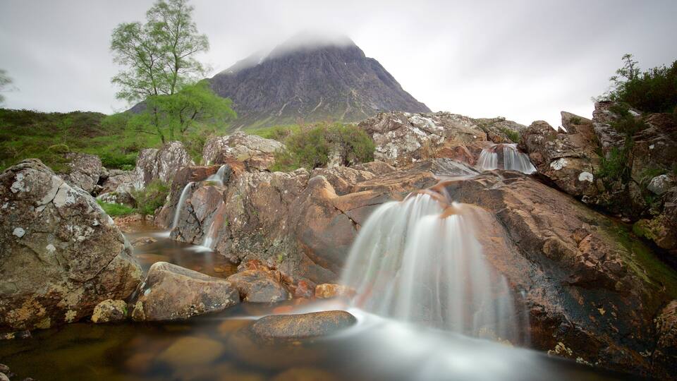 A waterfall cascading over rocks with a mountain in the background.