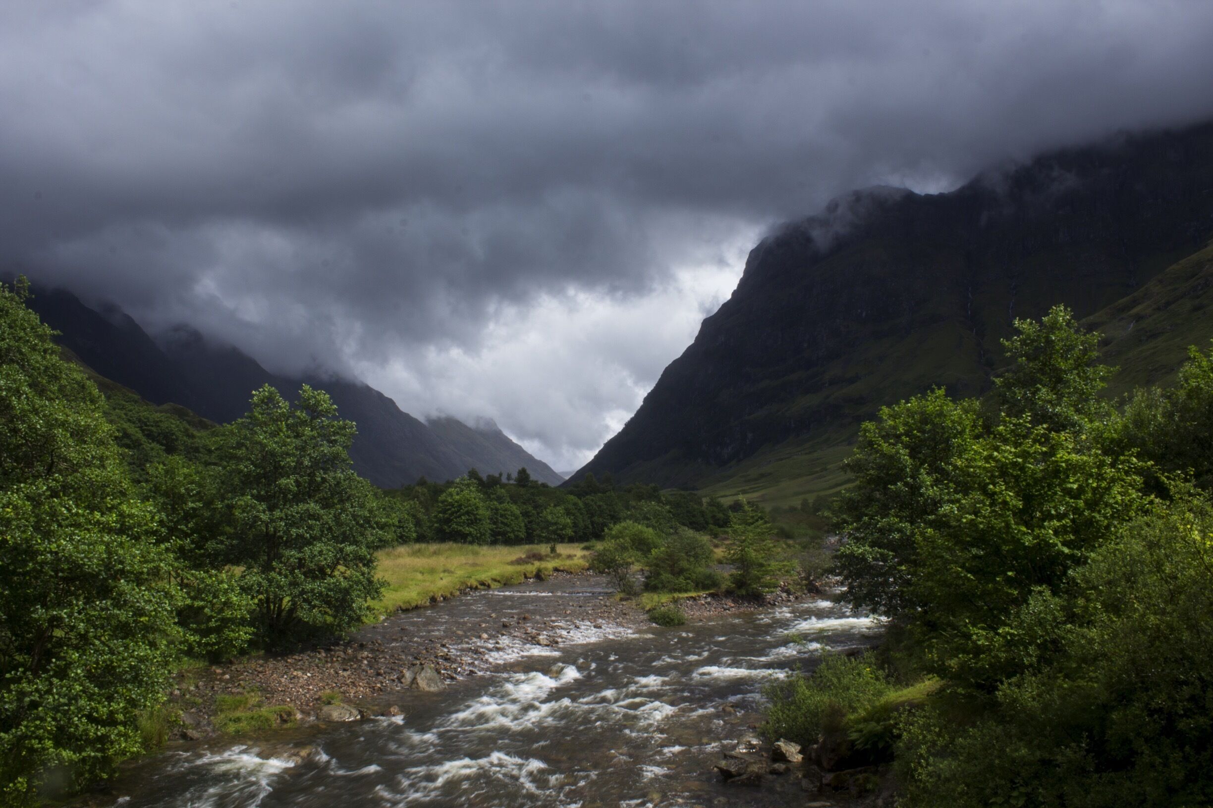 A river flowing through a valley with lush greenery and mountains in the background.
