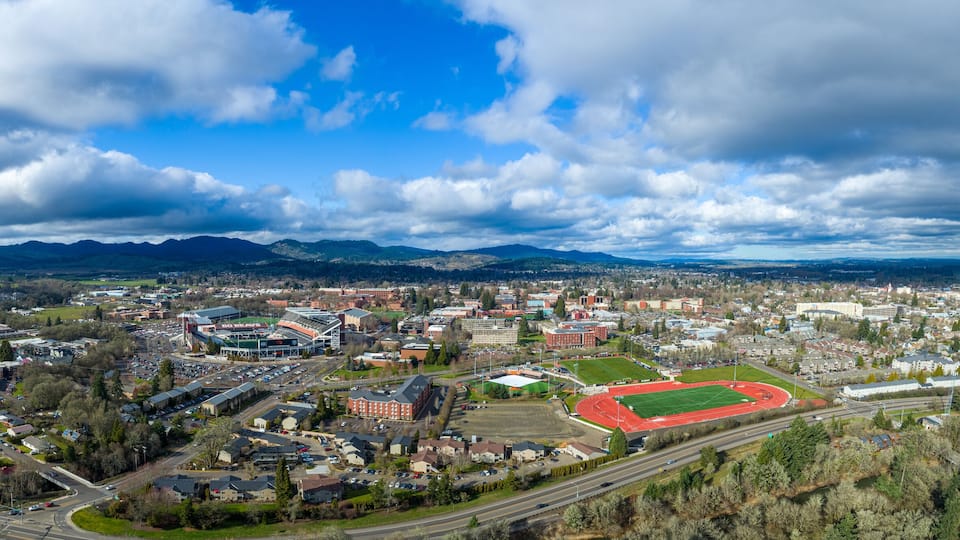 An aerial view of a town with a large stadium, roads, and surrounding mountains.