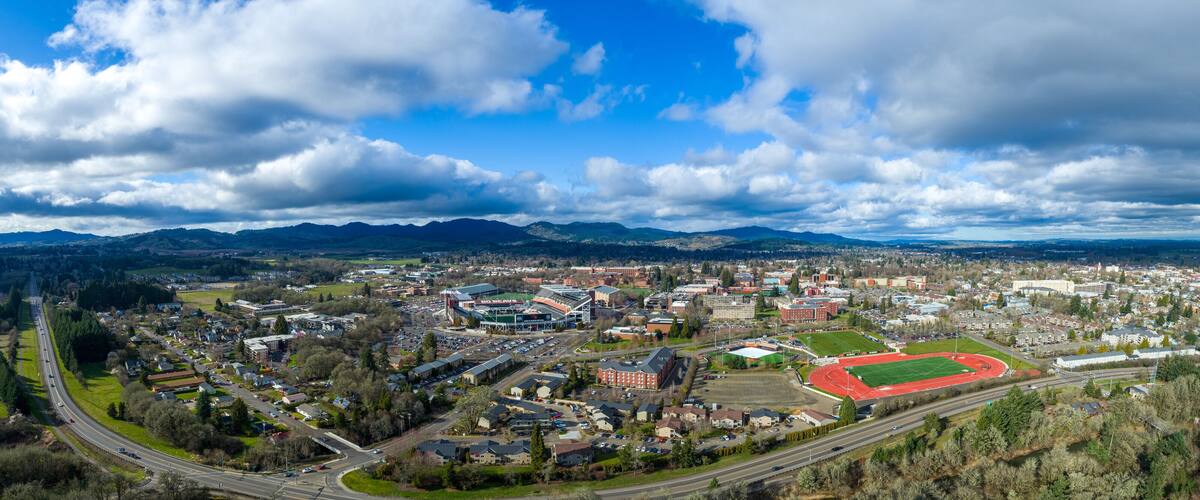 An aerial view of a town with a large stadium, roads, and surrounding mountains.