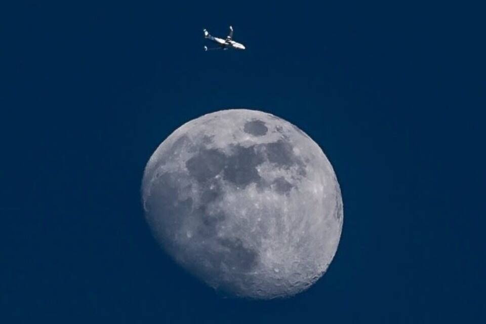 Una luna grande con un avión volando en el cielo.