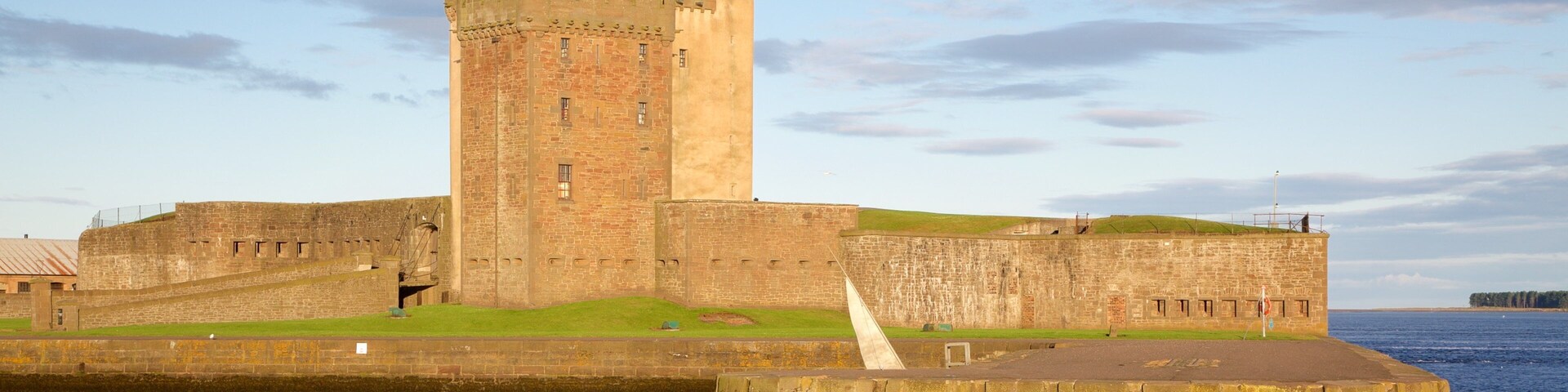 Un castillo de piedra histórico con una torre destacada, ubicado junto a un cuerpo de agua.