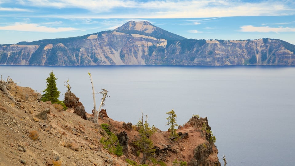 A mountain range with a lake in the foreground and a forested peak in the background.