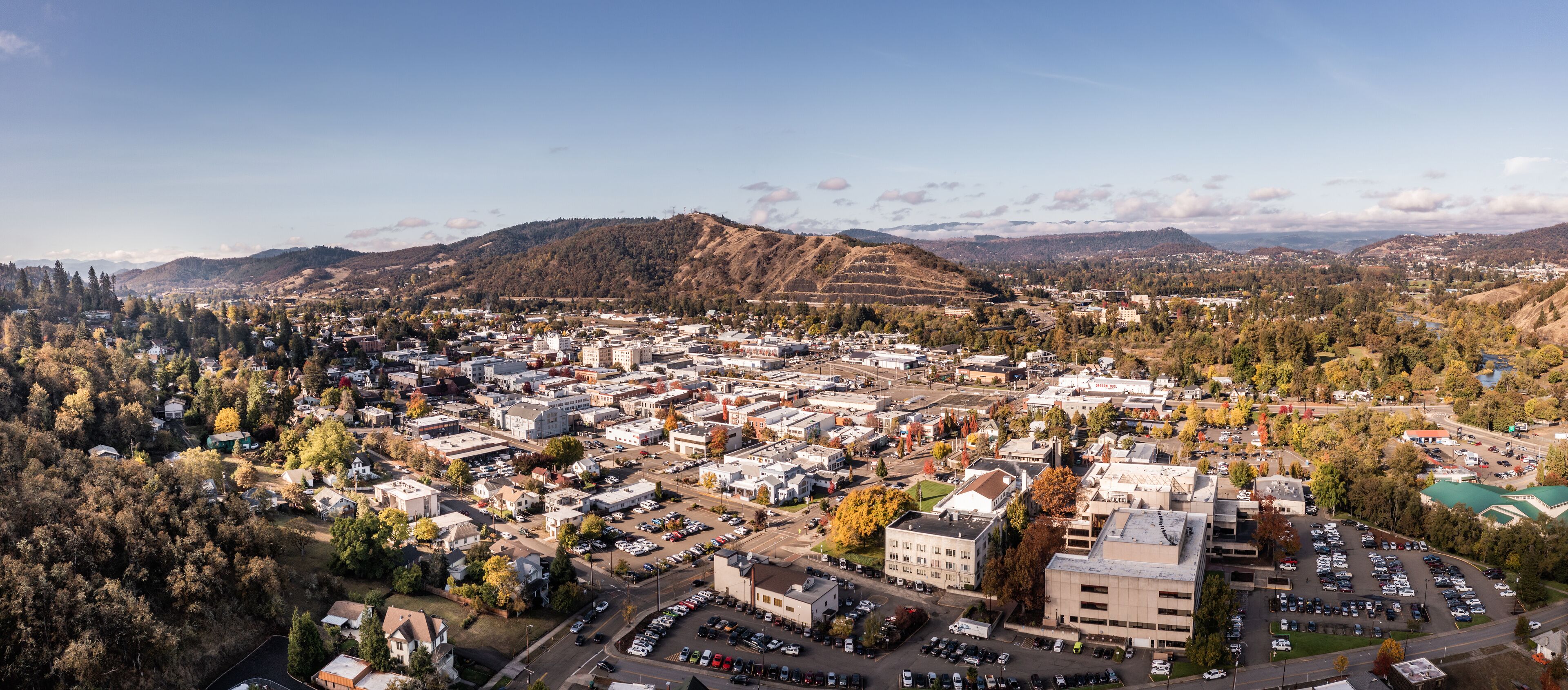 An aerial view of a town with a central business district, surrounded by hills and trees.