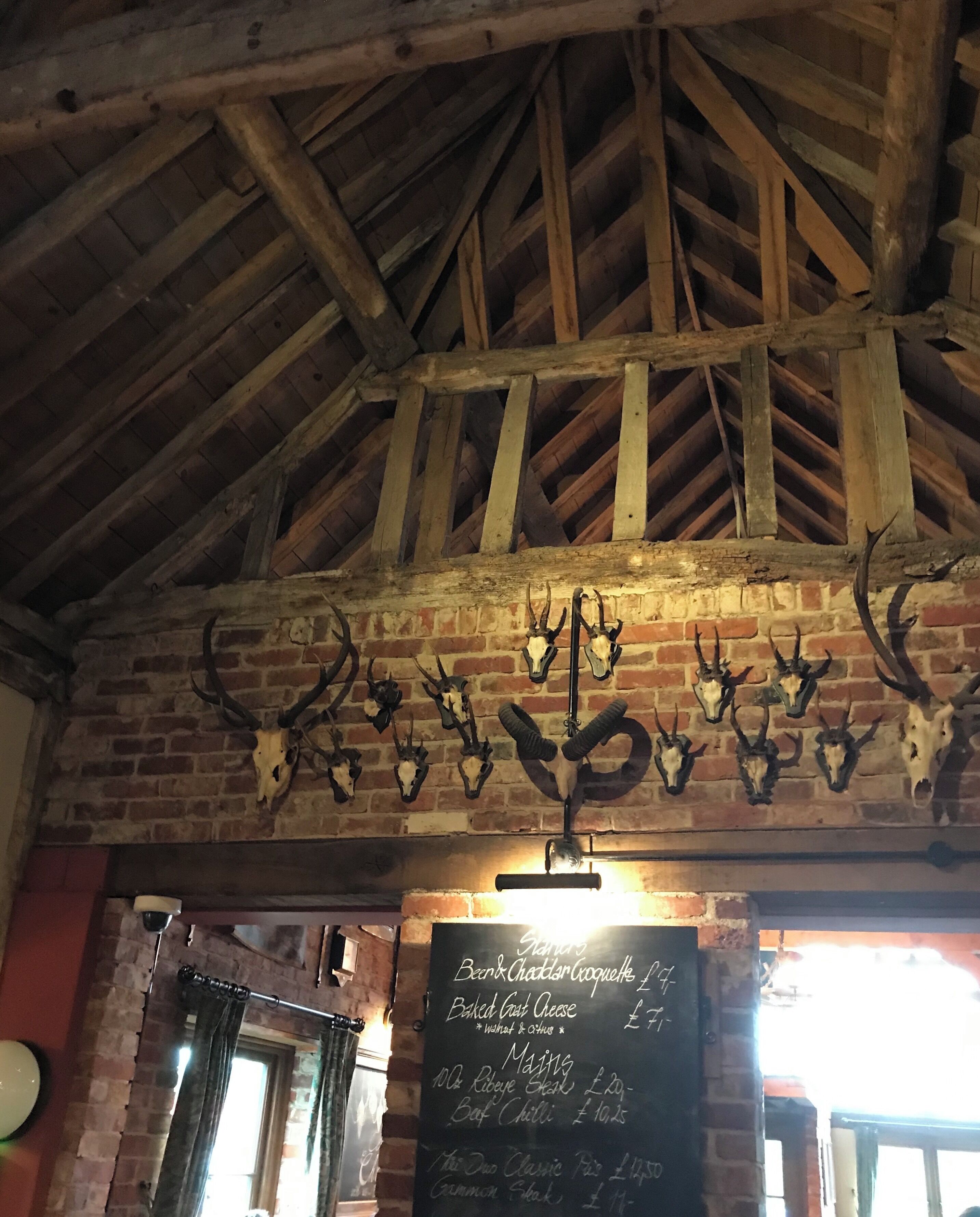 A rustic interior with exposed wooden beams, a brick wall, and mounted animal skulls. A chalkboard menu is visible.