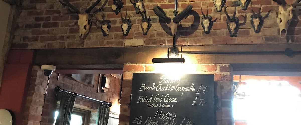 A rustic interior with exposed wooden beams, a brick wall, and mounted animal skulls. A chalkboard menu is visible.