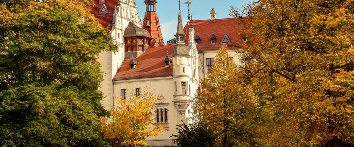 A historic building with red-tiled roofs and ornate spires, surrounded by autumn foliage.