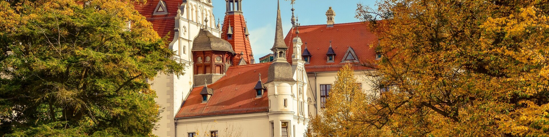 A historic building with red-tiled roofs and ornate spires, surrounded by autumn foliage.