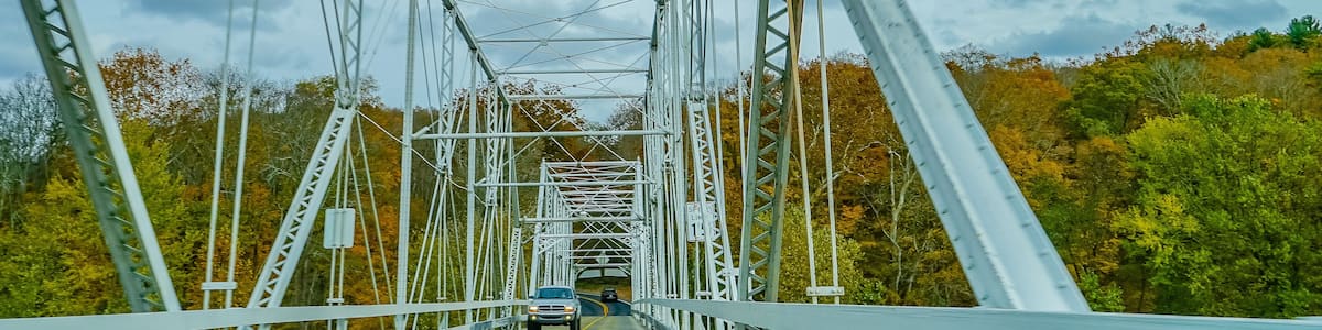 Eine Metallbrücke mit einer gelben Fahrbahnmitte, umgeben von Bäumen im Herbstlaub.
