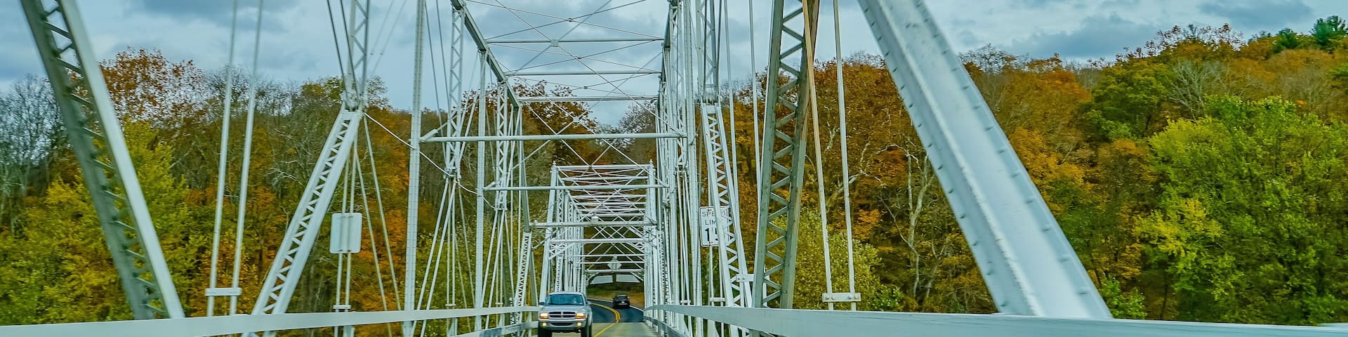 A metal bridge with a yellow centerline, surrounded by autumn-colored trees.
