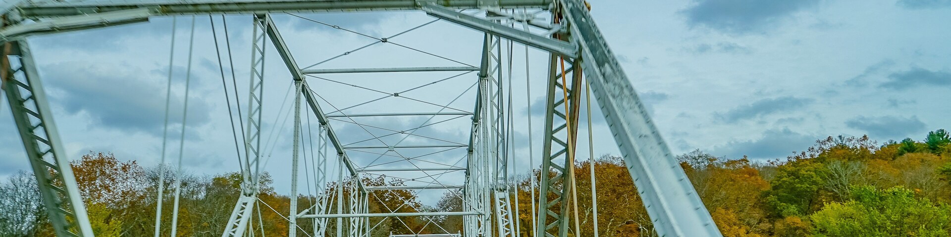 Un puente de metal con línea central amarilla, rodeado de árboles de colores otoñales.