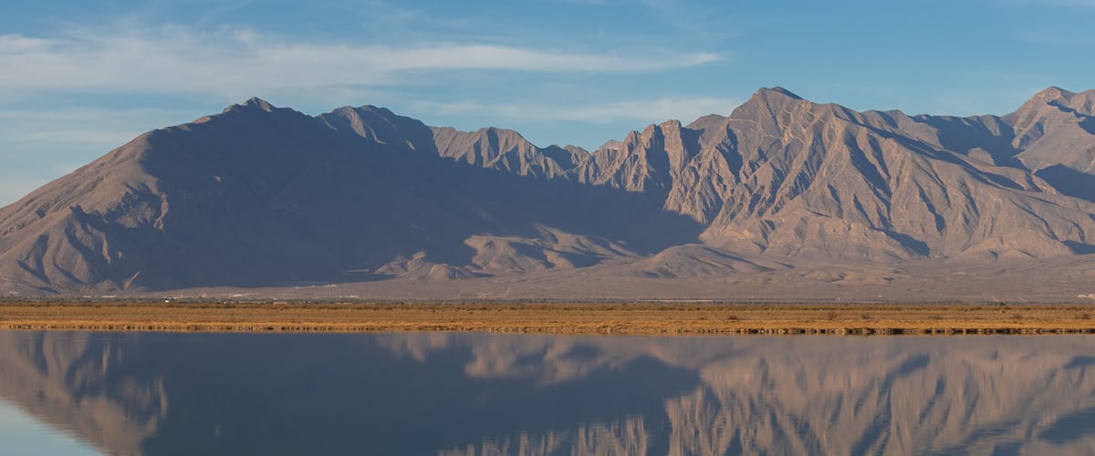 A mountain range reflected in a calm lake with a clear sky.
