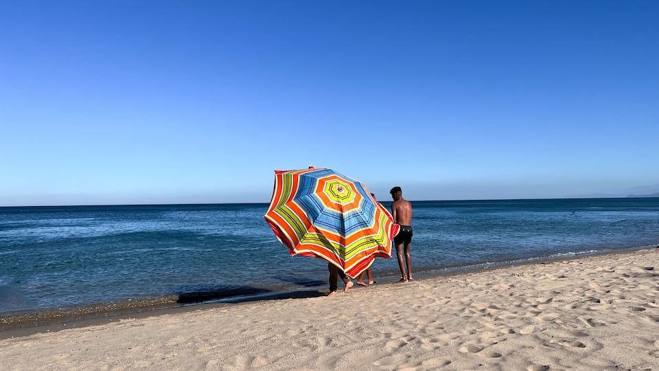 A beach with a person holding a colorful umbrella.