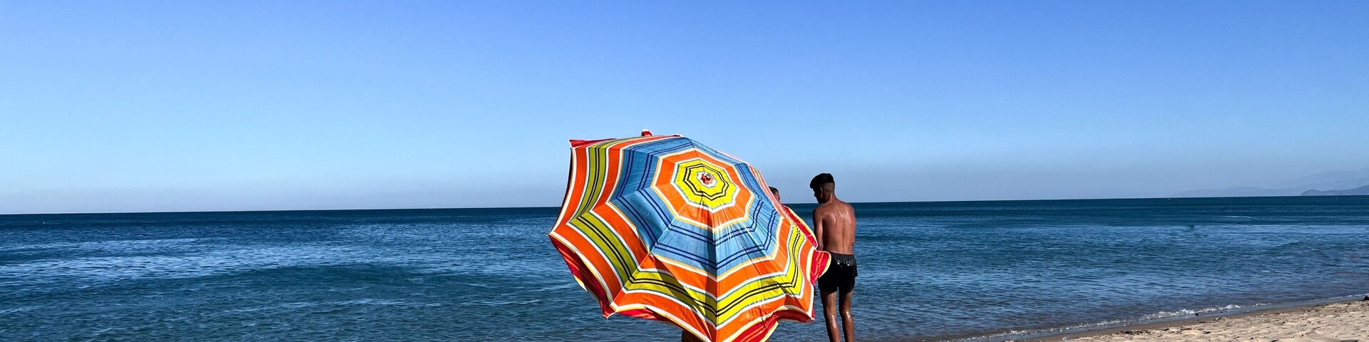 Una playa con una persona sosteniendo un paraguas colorido.