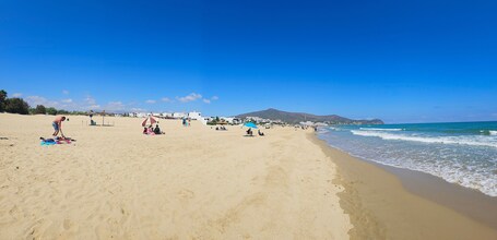 Ein sandiger Strand mit Menschen, die sonnenbaden, und ein Berg im Hintergrund.