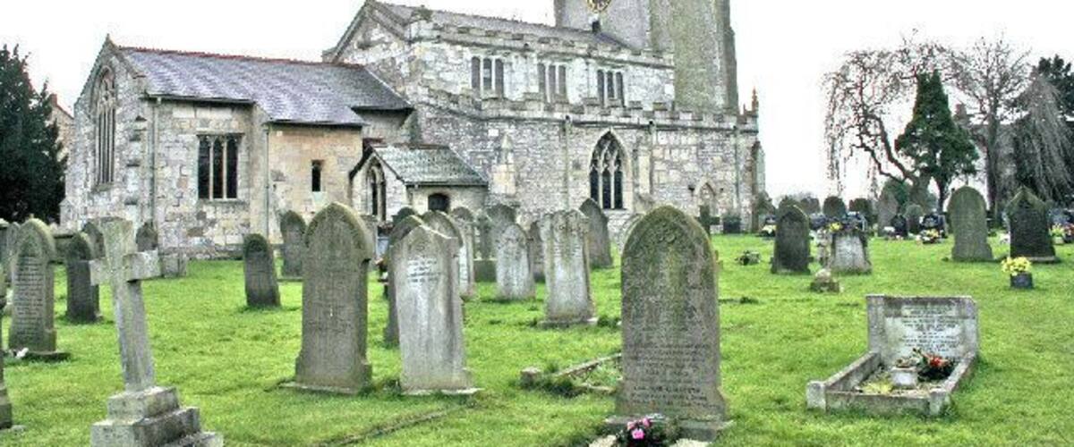 A church with a tall tower and a graveyard with numerous headstones.