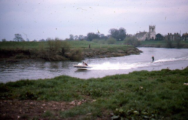 A river with a boat and a person wakeboarding. There is a building in the background.