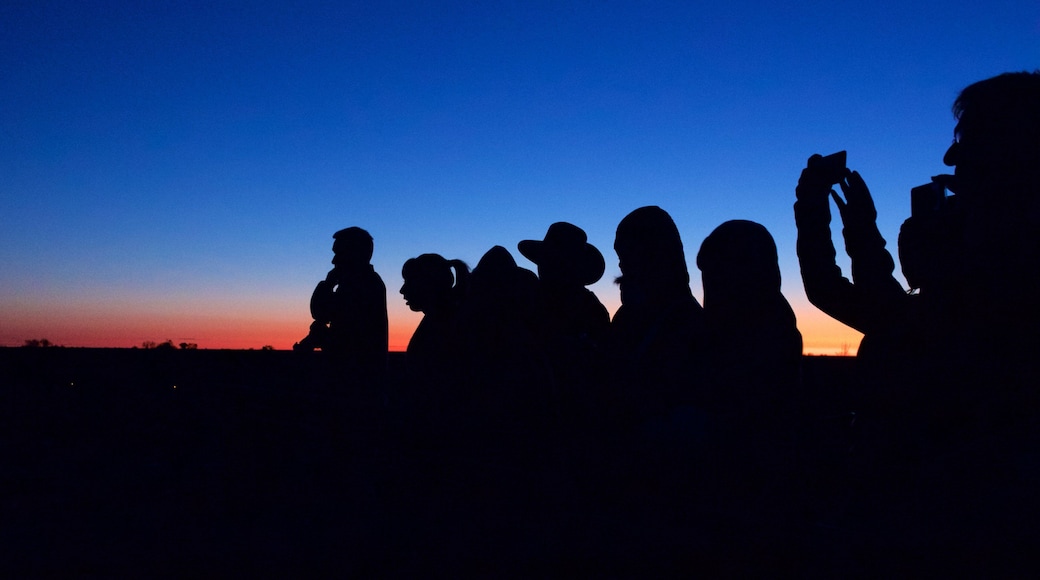 Uluru featuring desert views and a sunset as well as a small group of people