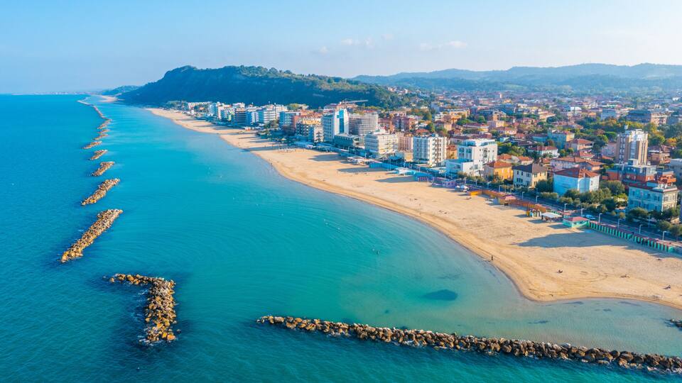 A coastal cityscape with a beach, buildings, and a rocky shoreline.