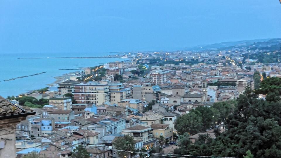 A coastal cityscape with buildings, a coastline, and a distant mountain range.