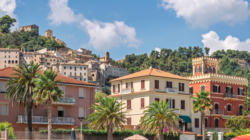 A coastal town with historic buildings, palm trees, and a hilltop castle.