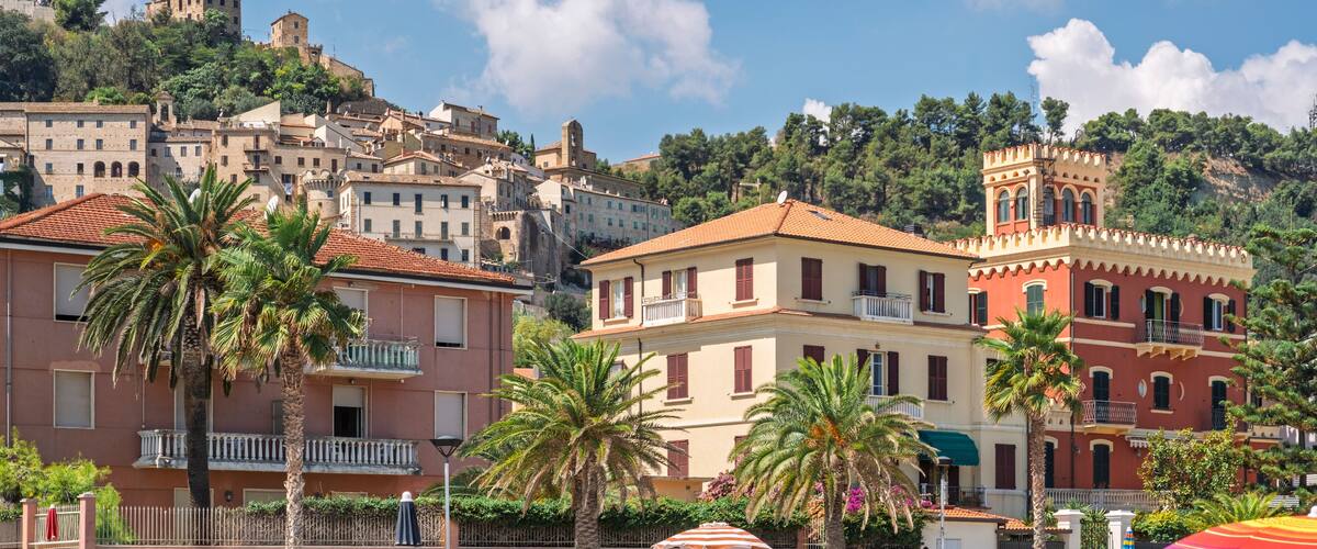 A coastal town with historic buildings, palm trees, and a hilltop castle.