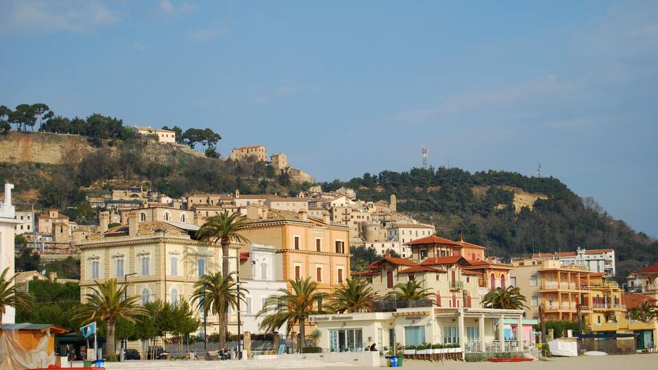 A coastal town with historic buildings, palm trees, and a hill with a castle-like structure.