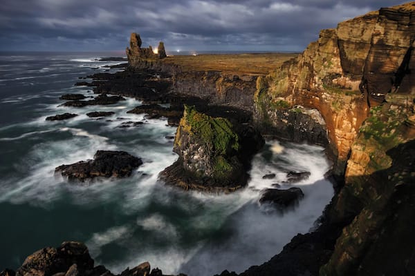 A rugged coastline with rocky formations and waves crashing against them.