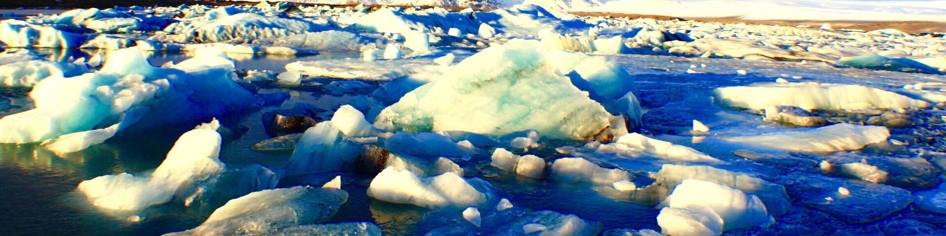 Un paisaje helado con icebergs dispersos y montañas nevadas bajo un cielo parcialmente nublado.