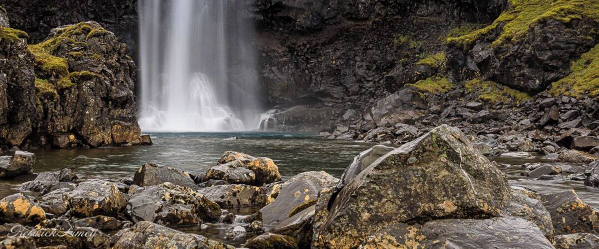 Una cascada se precipita en una poza rocosa rodeada de acantilados escarpados.