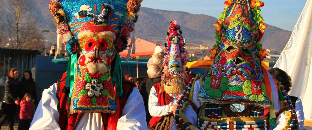 Two individuals wearing elaborate, colorful traditional masks and beaded necklaces.