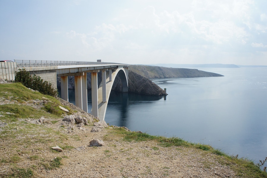 A bridge over a calm body of water with a hilly landscape in the background.