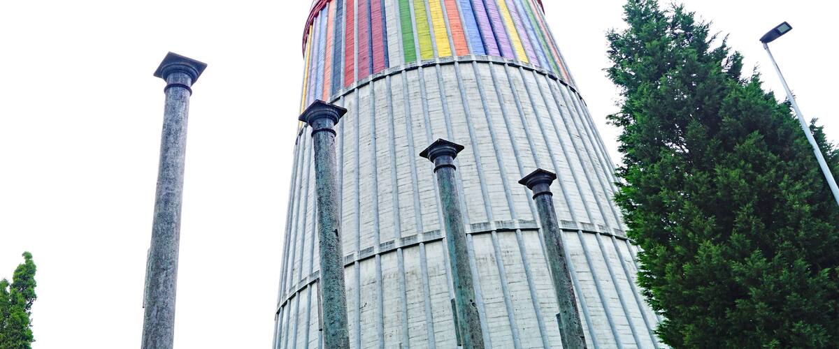 A tall, cylindrical structure with a rainbow-colored top and three columns at the base.