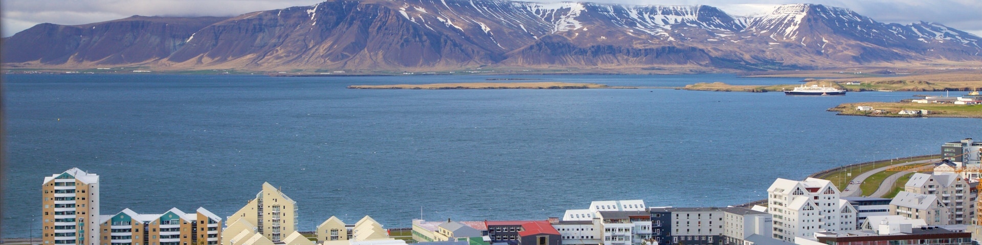 A coastal town with colorful buildings, a large body of water, and snow-capped mountains in the background.