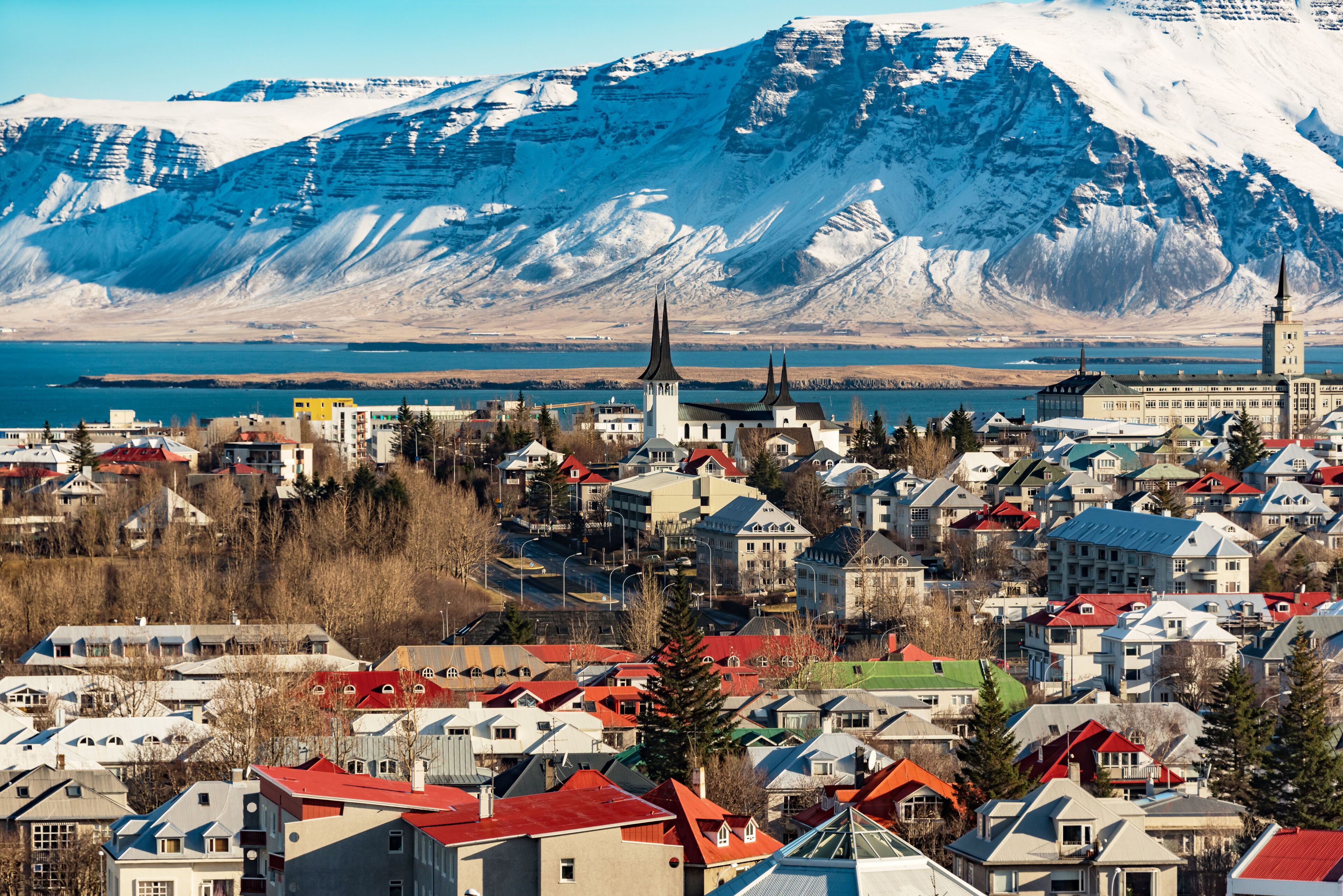 A town with snow-covered mountains in the background and a church with a tall spire in the foreground.
