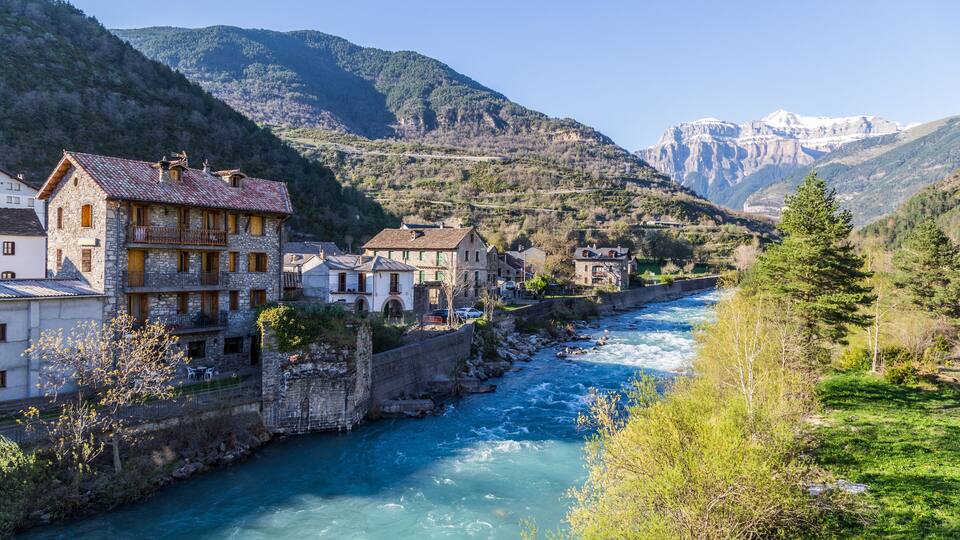 A river flowing through a town with stone buildings and mountains in the background.