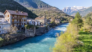 Un río serpentea por un pueblo con edificios de piedra y montañas al fondo.