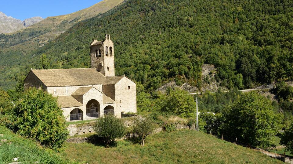 A stone church with a bell tower surrounded by lush green hills and a clear blue sky.