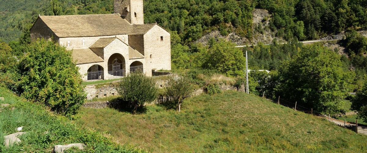 A stone church with a bell tower surrounded by lush green hills and a clear blue sky.