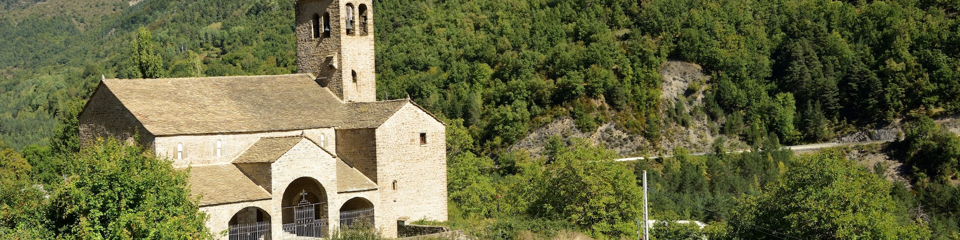 A stone church with a bell tower surrounded by lush green hills and a clear blue sky.