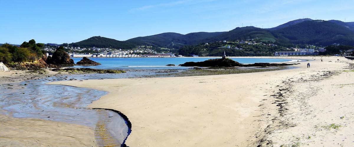 A beach with clear skies, distant mountains, and a coastal town.