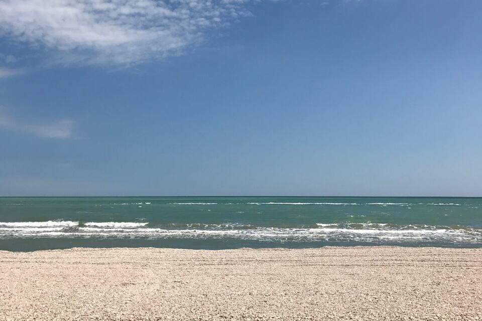 Uma praia com areal de pedras, céu azul límpido e algumas nuvens esparsas.