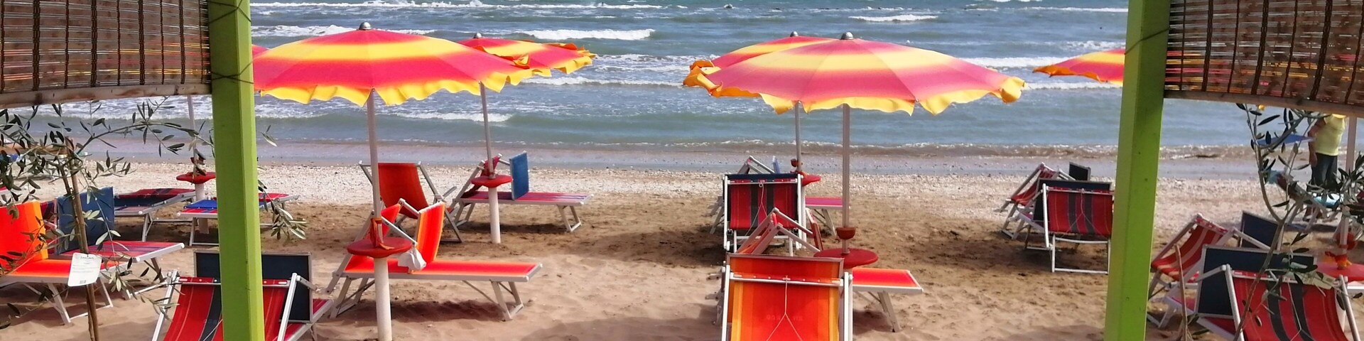 Un pabellón frente a la playa con toldos a rayas y sillas de playa a rayas rojas y blancas.