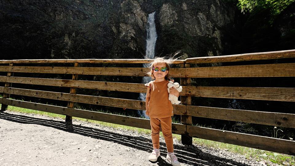 Funny baby girl in sunglasses against waterfall in Liechtensteinklamm or Liechtenstein Gorge, Austria.