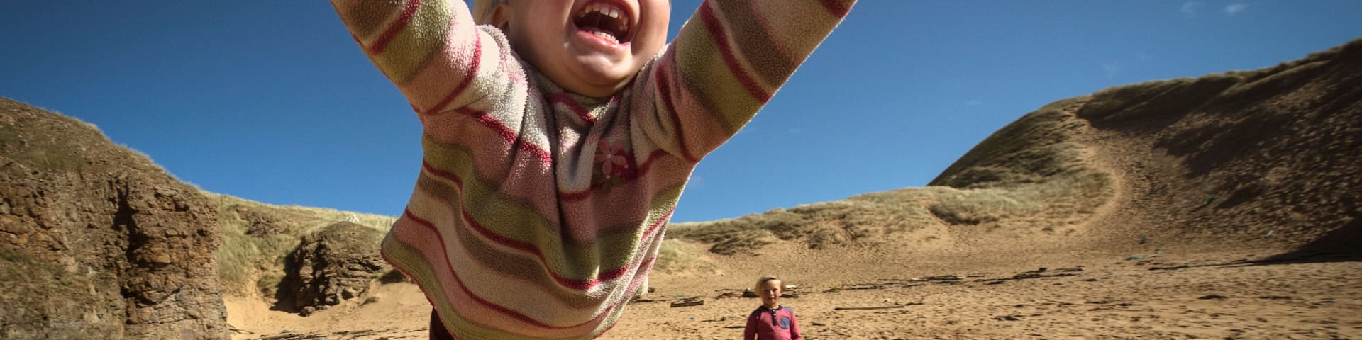 Parent holding daughter's hands, spinning her around, young son in background, low angle view, Lahinch, Clare, Ireland