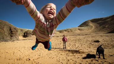 Parent holding daughter's hands, spinning her around, young son in background, low angle view, Lahinch, Clare, Ireland